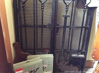 Photo showing black metal fireplace screen with mesh and twisted bar design along with fireplace tools including brush, poker, and shovel with decorative handles.