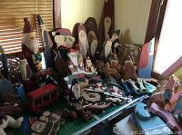 Wide view of the Santa themed wood crafts on a table showing multiple wooden Santa figures, gingerbread men, and other holiday shapes.