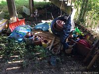 Wide view of lot showing stacked terracotta pots, bag of potting soil, garden seat, and hanging bracket under porch stairs