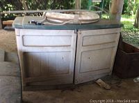 Plastic Suncast deck box exterior with green lid and beige body showing wear and outdoor dirt, placed on a dirt ground.