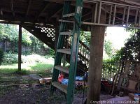 Green 6-foot fiberglass step ladder standing in a shaded outdoor area under a wooden structure.