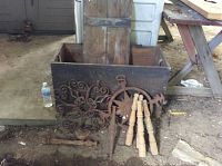 Antique wooden box with detached lid and cast iron decorative elements placed inside and around it, along with wooden spindles.
