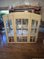 Front view of cream painted curio cabinet with glass doors and shelves visible