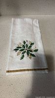 Front view of towel showing holly embroidery and gold border