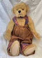 Front view of tan plush teddy bear wearing corduroy overalls