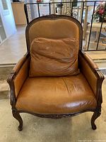 Front view of leather armchair showing seat and back cushion, carved wood frame and nailhead trim
