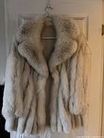 Front view of ivory/cream real fur coat on hanger