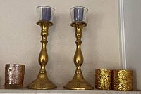 Front view showing both brass candlesticks with glass cups, purple candles, extra glass votive holder and gold glitter candles