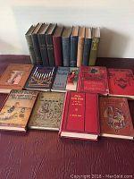 Front and top view of 19 antique hardcover books laid out in two rows with varied cover colors and conditions.