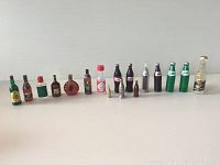 Full array of 17 miniature vintage advertising bottles showing assortment of brands, styles, and materials.