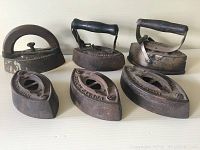Six antique cast sad irons including three with wooden handles and three without handles, showing various sizes and styles.
