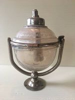 Front view of antique glass soap dispenser showing spherical shape, metal swivel mount, and pump top.