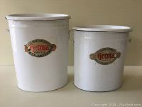 Front view of two vintage white porcelain enamel containers with German labels, different sizes.