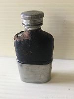Front view of antique pewter hip flask covered partially in black leather with some wear and screw top lid.