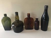 Front view of five antique colored glass bottles of various sizes and shapes against a light background.