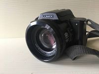Front view of Panasonic Lumix camera showing lens with Leica branding and 12x optical zoom marking.