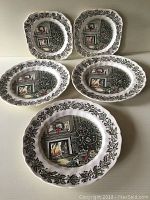 Five vintage collectible plates arranged in two rows showing Victorian Christmas living room scene with fireplace, decorated Christmas tree, wrapped gifts, and holly leaf border pattern.