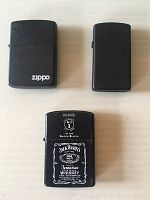 Top view of all three lighters: two black Zippo lighters and one Jack Daniel's advertising lighter with white logo and text.