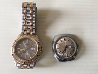 Two wristwatches shown side by side on flat surface, Pulsar with bracelet and Timex head only.