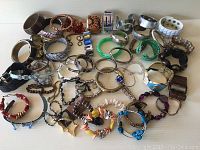 Overview of 55 assorted costume bracelets in various styles including metallic bangles, beaded bracelets, and fabric wristbands.