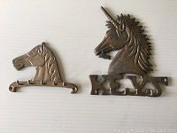 Two vintage brass wall mount key holders lying flat showing side profiles and hooks.
