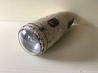 Side angled view of vintage white metal bicycle light showing clear convex glass lens, black on/off switch, and worn paint