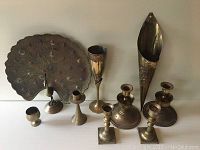 Nine pieces of vintage brass including two sets of candle holders, a chalice, a brandy cup, wall flower holder, and peacock.