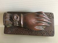 Front view of the hand-shaped brass door knocker mounted on rectangular backplate with decorative border pattern.