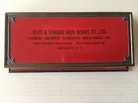 Closed rectangular red metal box with brass-toned trim and black printed Ross & Howard Iron Works Co., Ltd. branding on the lid.