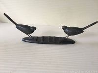 Full view of wood carving showing two black birds with white beaks on a grooved base