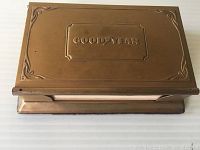 Top view of closed brass box with embossed Goodyear logo and decorative corners.