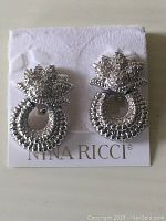 Front view of Nina Ricci silver tone earrings showing detailed textured circular and floral-like design.