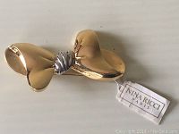 Front view of gold-tone bow brooch with silver-tone twisted knot center and Nina Ricci Paris tag attached.