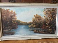 Full view of the framed oil painting showing a river and autumn trees.