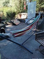 Full view of multicolor striped hammock hanging on dark blue metal stand outdoors