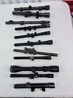 Ten rifle scopes laid out showing overall quantity and variety