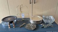 Group shot of chargers, crystal pieces, utensils, cake stand, trivet and easel stand