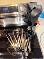 Utensil holder with black nylon utensils and several stainless tongs on stovetop