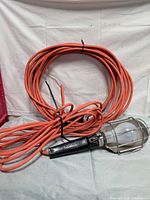 Coiled orange extension cord with attached shop light showing overall lot