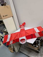 Full view of red and white nylon airplane windsock laid flat showing wings, fuselage and intake opening