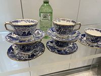 Front view showing five cup and saucer pairs with blue/white pattern and gold edging