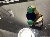 Ring front view showing blue center and green cabochons with coin for scale