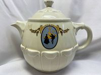 Front view of cream ceramic teapot with cameo and gold accents