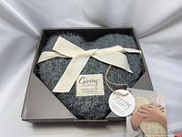 Top view of gray faux fur heart with ribbon in box, hang tag visible