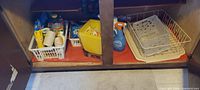 Cabinet interior showing baskets with cleaning supplies, twine and yellow storage bin