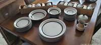 Full dinnerware set on table showing plates, bowls, boxed cup & saucer sets, creamer and sugar bowl