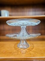 Both pressed glass cake stands stacked to show pedestal bases and plate profiles