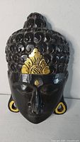 Front view of carved wooden Buddha face mask showing design and gold accents