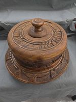 Angled view of carved wooden cake plate with lid showing knob and base