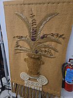 Full view of tapestry showing urn, foliage, scroll base and fringe